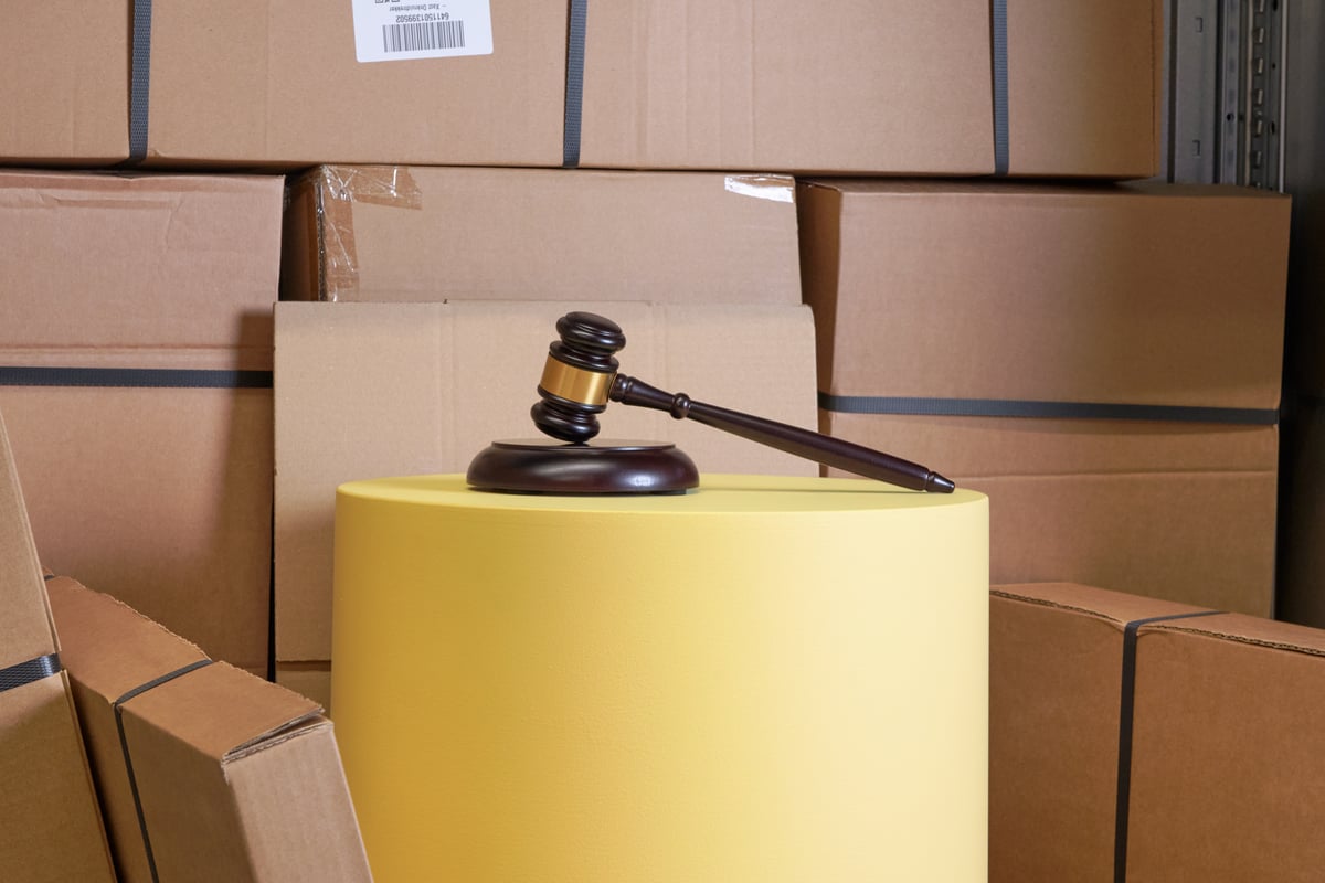 A judge's gavel rests on a yellow cylinder, surrounded by stacks of brown cardboard boxes.
