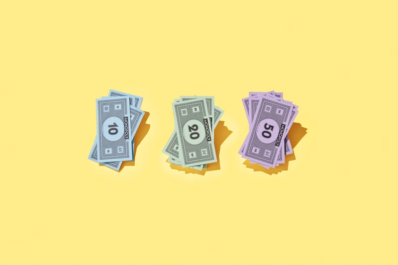 Stapel von blauem, grünem und lila Monopoly-Geld sind ordentlich auf einem leuchtend gelben Hintergrund angeordnet.