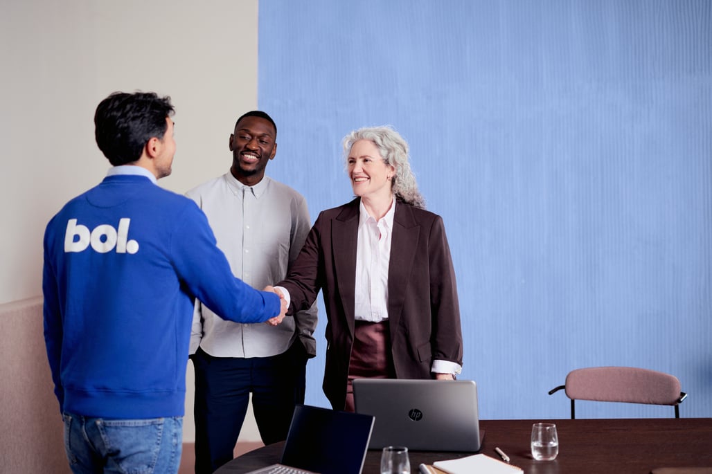 Zwei Personen schütteln sich in einem professionellen Besprechungsraum die Hände, was eine Einigung oder Zusammenarbeit symbolisiert.