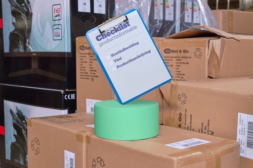 Clipboard with checklist about content on a green stand, placed on stacked cardboard boxes.