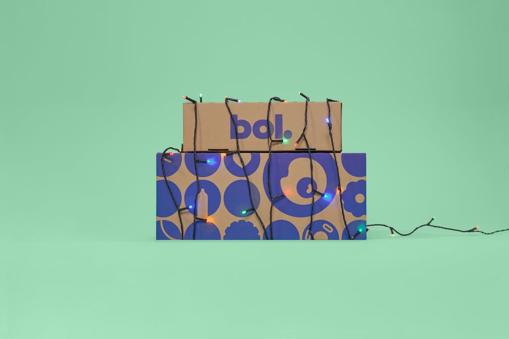 Cardboard boxes stacked against a mint green background, wrapped with colorful fairy lights.