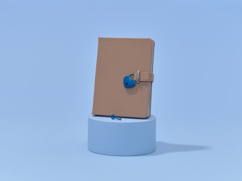 A beige diary with a blue heart-shaped lock stands upright on a light blue cylindrical platform against a matching blue background.
