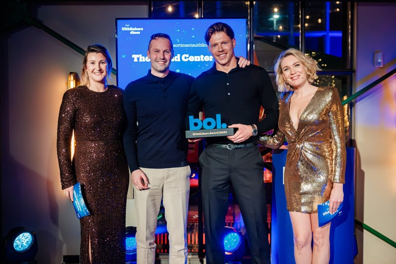 Four people are smiling at an awards ceremony. The two men in the middle are holding a ‘bol.com’ award. The two women on the sides are wearing glitter dresses.