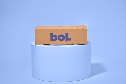 A brown cardboard box with the bol logo on a light blue cylindrical platform against a matching light blue background.