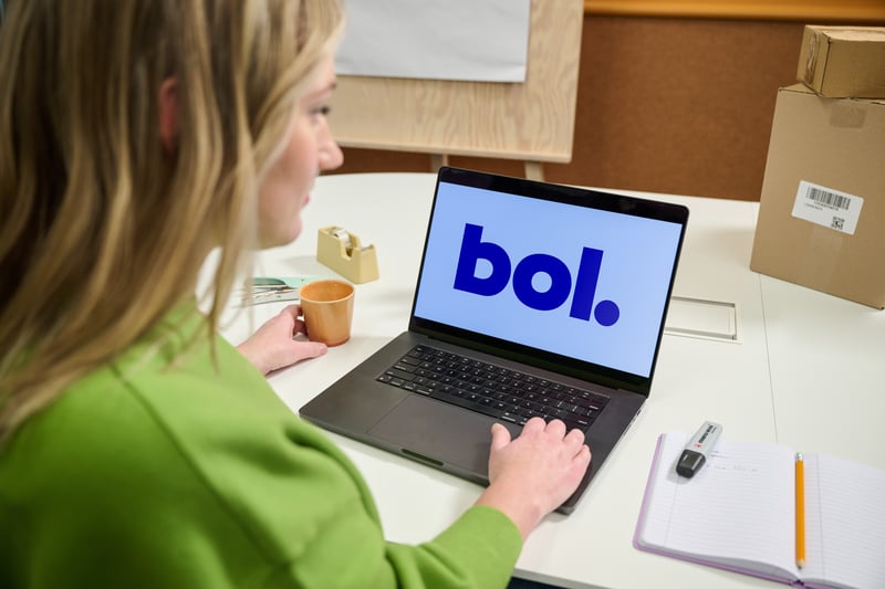 A person in a green shirt works at a laptop displaying the "bol" logo.