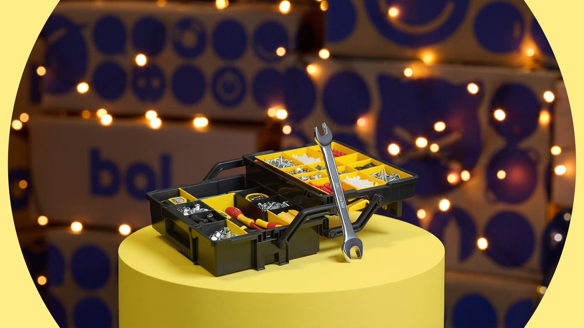 A black toolbox with assorted tools and screws sits open on a yellow podium