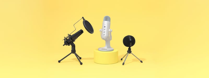 Drie microfoons staan voor een gele achtergrond. In het midden staat een grote witte microfoon op een standaard, met aan beide kanten zwarte microfoons op statieven. 