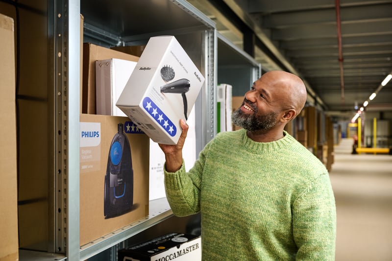 Een man staat in een magazijn en houd een doos met een fohn vast.