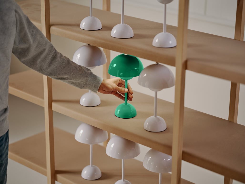 Cette image montre une étagère avec des lampes blanches. Une main tendue vers une lampe verte.