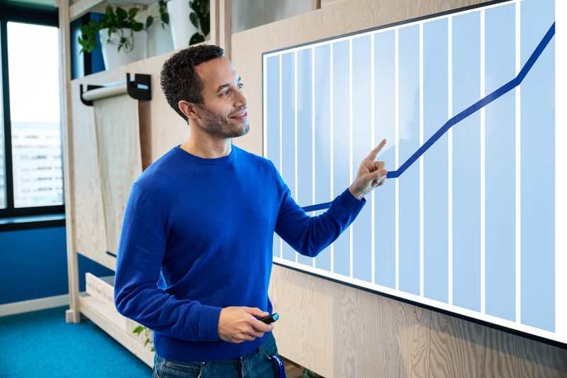 A man stands in front of a screen with an upward trend.