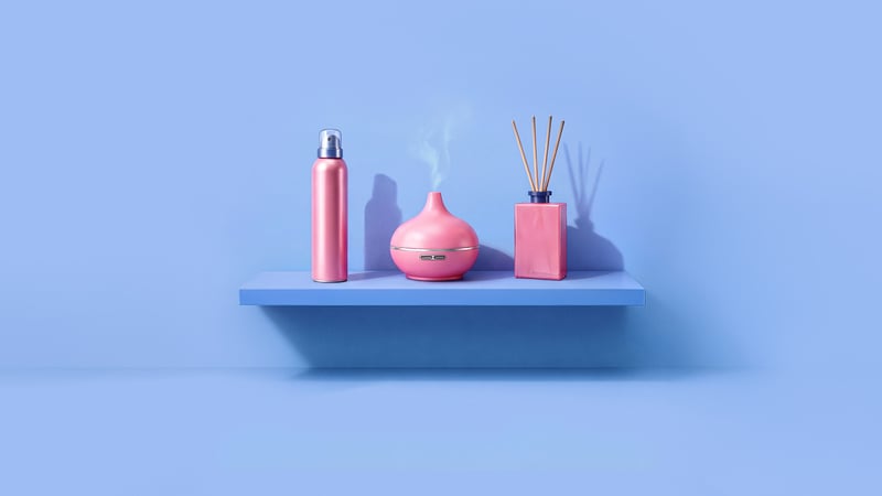 Een blauwe plank met daarop een roze douche schuim fles, een dampende roze aromadiffuser en een roze geurdiffuser.