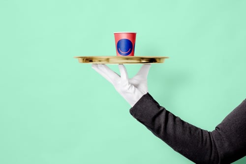 A person in a suit holds a tray with a red cup