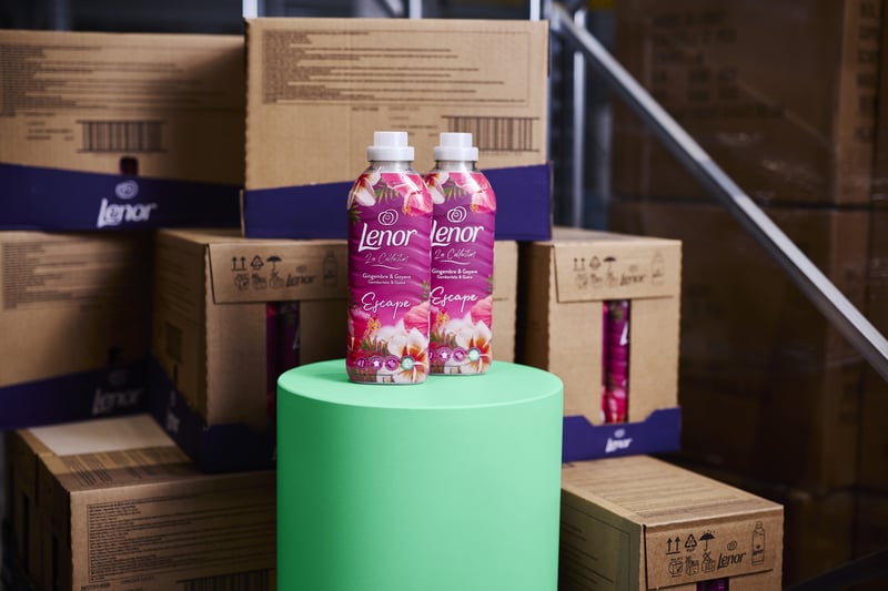 Two bottles of detergent are on a green cylinder, surrounded by stacked brown boxes in a warehouse setting.