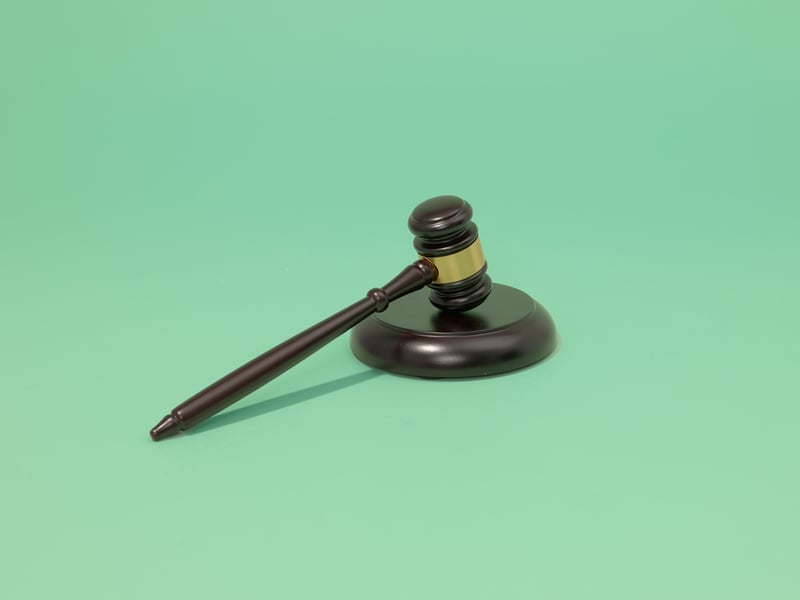 A wooden gavel lies diagonally on its block against a plain green background, symbolizing law and justice.
