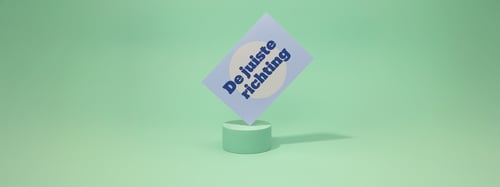 Groene achtergrond waarop een blauwe kaart met de tekst 'de juiste richting' zichtbaar op is