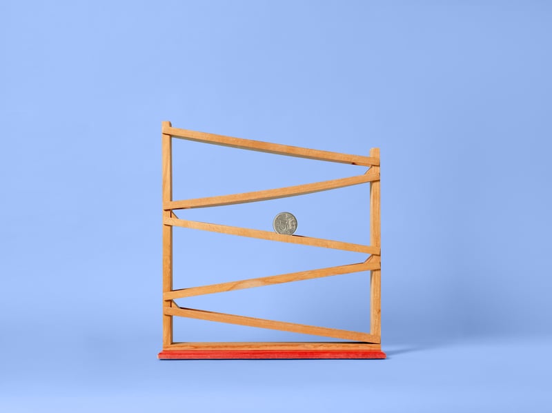 Een houten knikkerbaan op een blauwe achtergrond, met zigzagbanen en een oranje basis. Een enkele knikker rolt naar beneden.