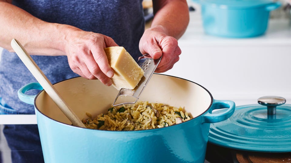 Persoon die kaas raspt boven een braadpan